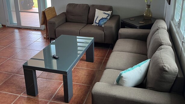 A living room with a sofa, a glass coffee table, and a ceiling fan.