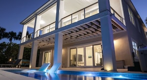 A modern two-story house with a swimming pool, large windows, and a covered patio area.