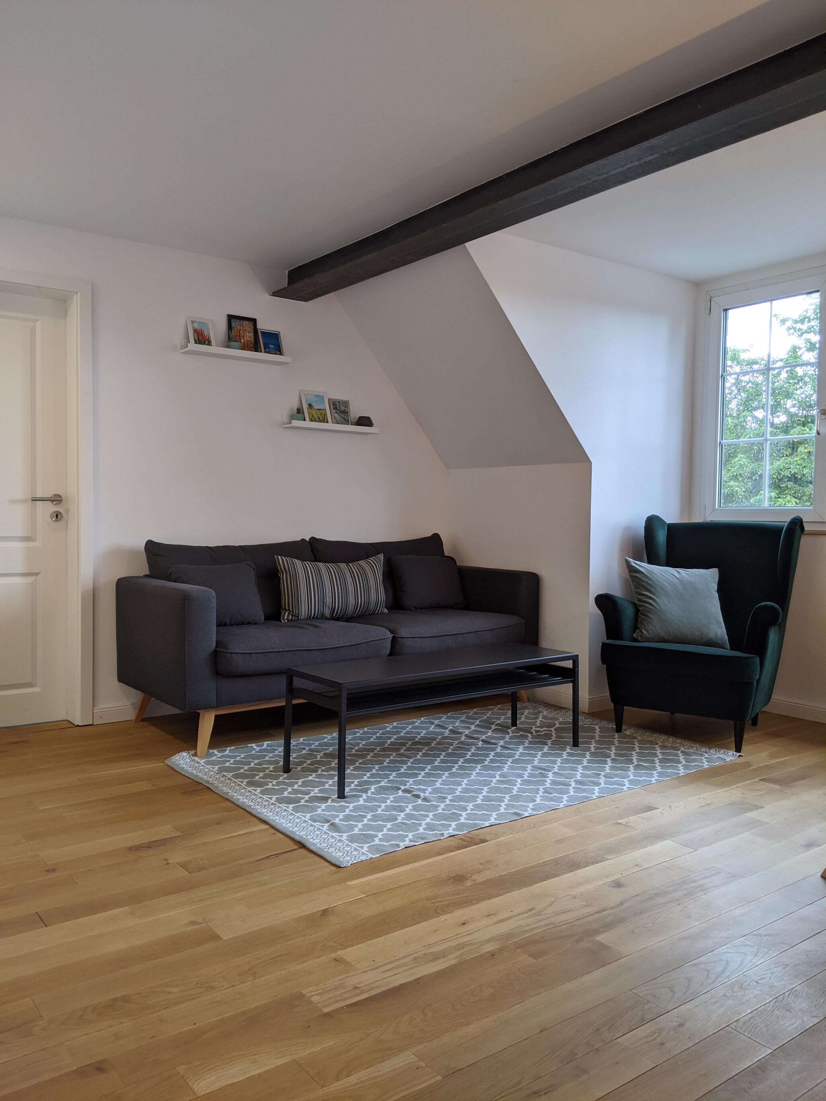 Een moderne woonkamer met een donkergrijze bank, een bijpassende fauteuil en een kamerkleed met een patroon.