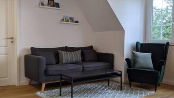Een moderne woonkamer met een donkergrijze bank, een bijpassende fauteuil en een kamerkleed met een patroon.