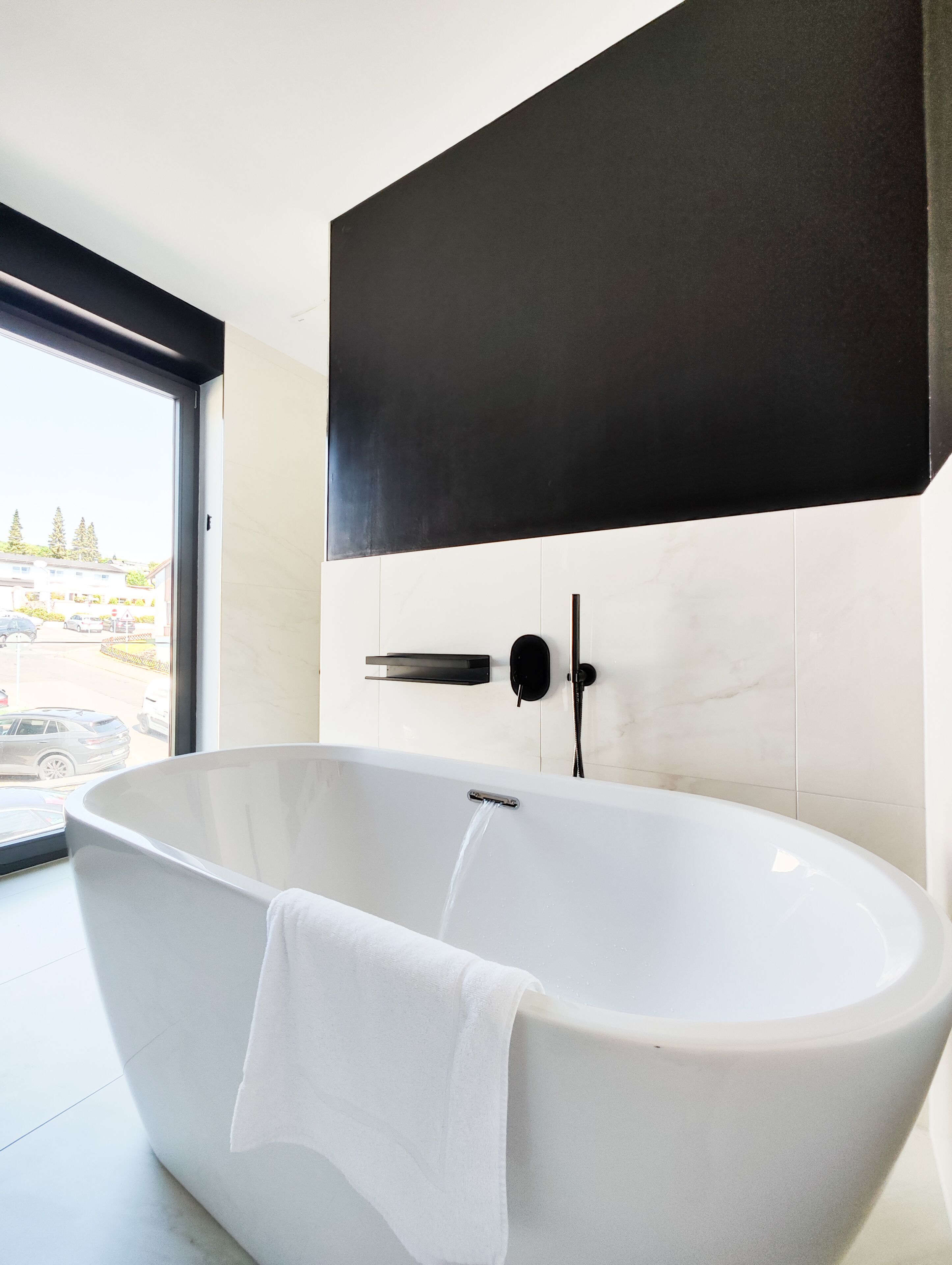Ein modernes Badezimmer mit einer freistehenden Badewanne, einem schwarzen, wandmontierten Waschbecken und Blick ins Freie durch ein großes Fenster.