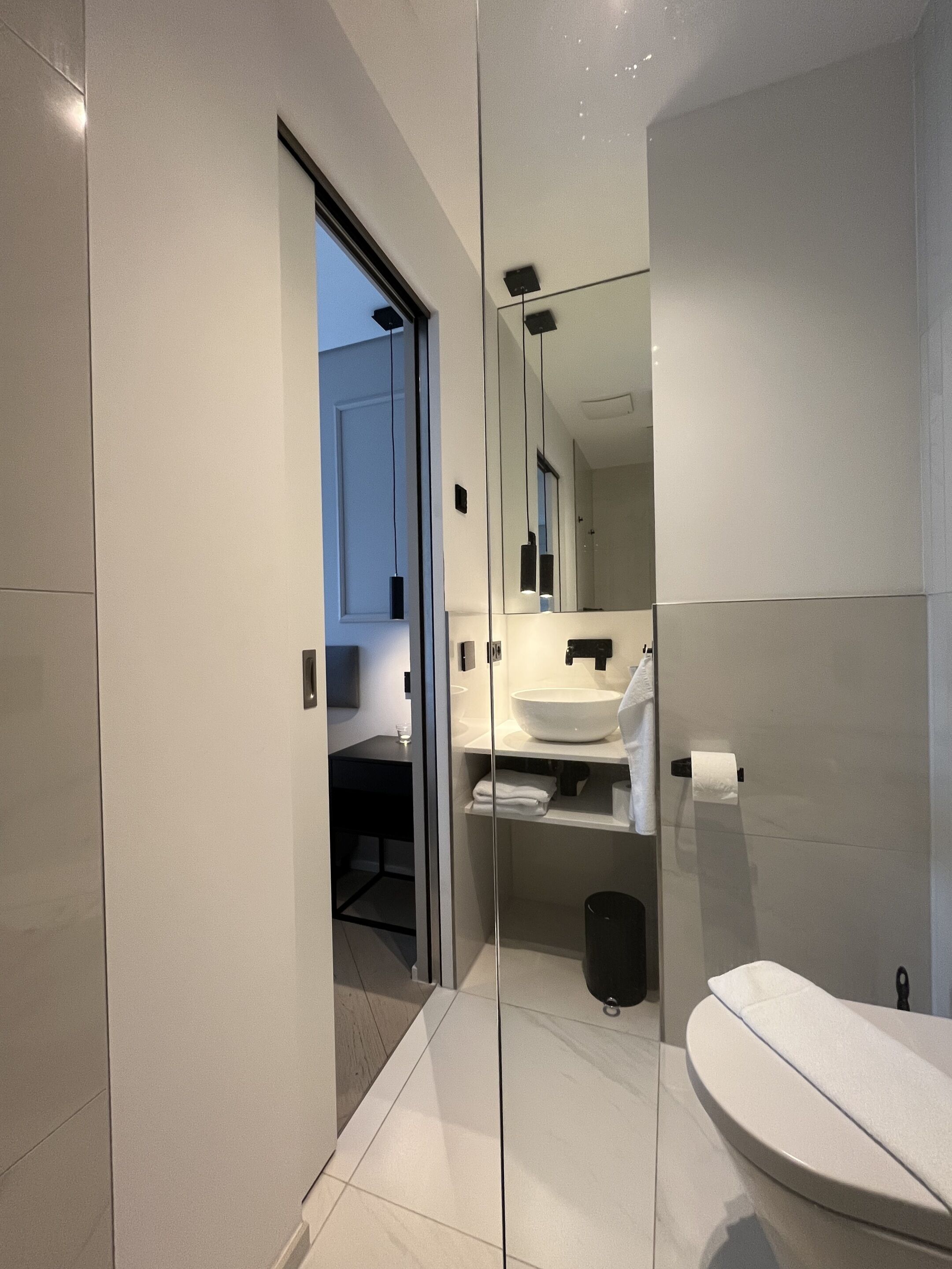 A modern bathroom with a glass partition, a large mirror, a white sink, and a toilet.