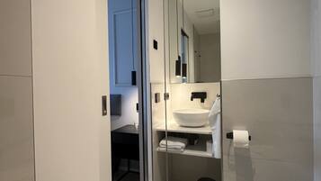 A modern bathroom with a glass partition, a large mirror, a white sink, and a toilet.
