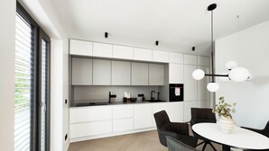 Een moderne keuken met witte kasten, een zwart aanrecht en een inbouwoven. Er is een eethoek met een ronde tafel en stoelen, en een hanglamp boven de tafel.