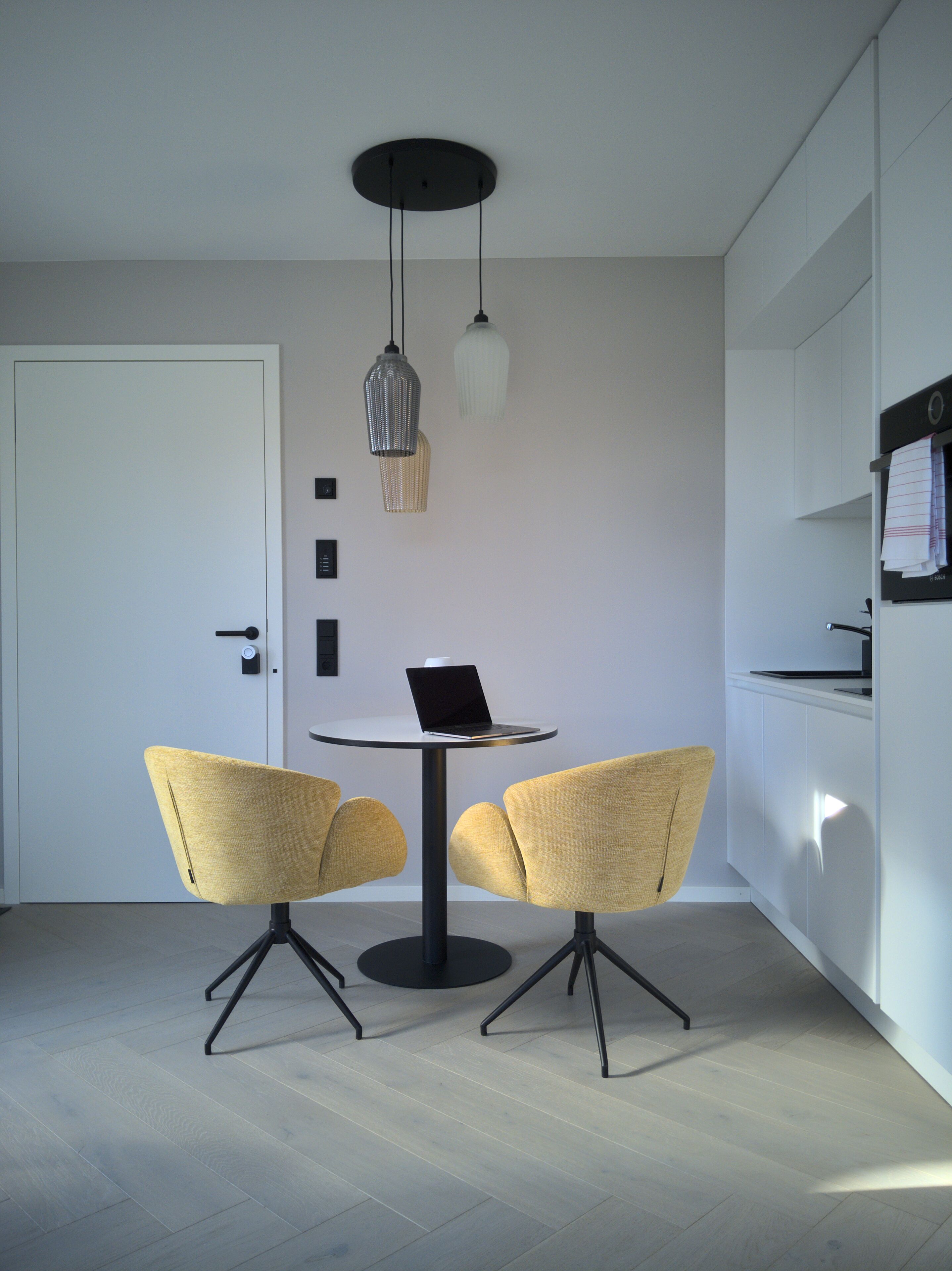 Una cocina moderna con una mesa redonda, dos sillas e iluminación colgante.
