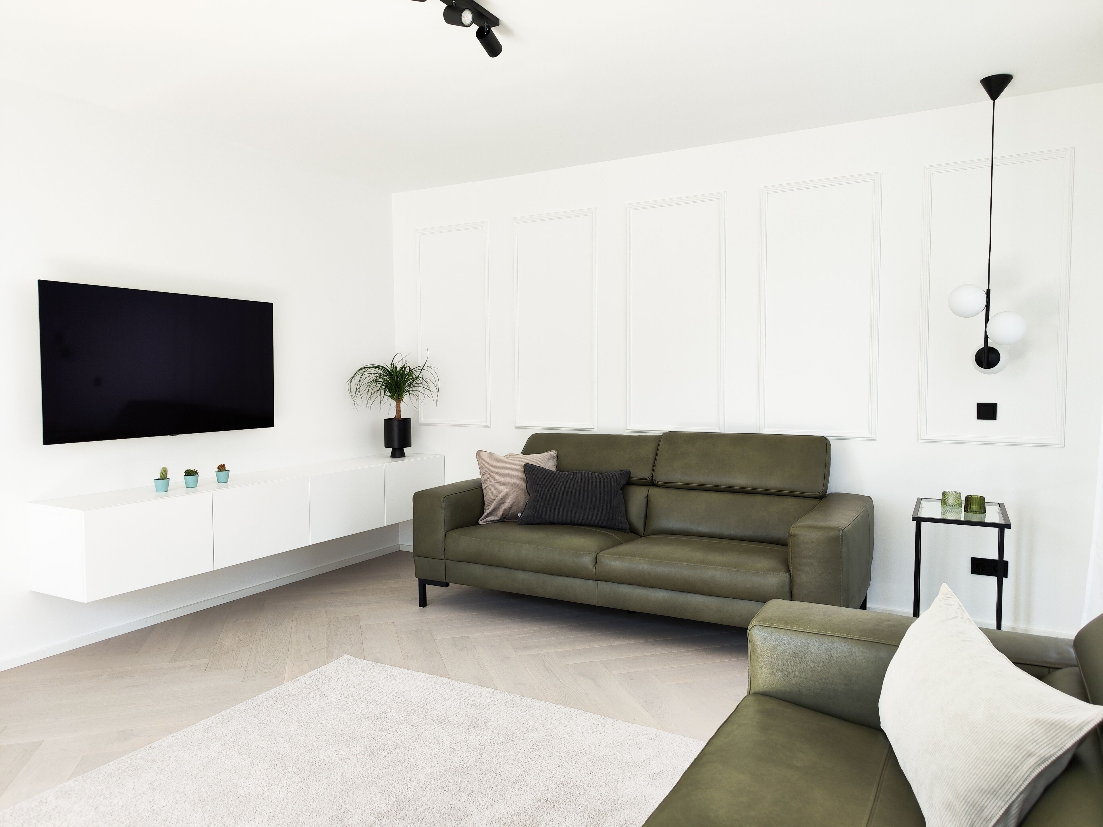 A modern living room with a large flat-screen TV, a green sofa, a small side table, and a potted plant.