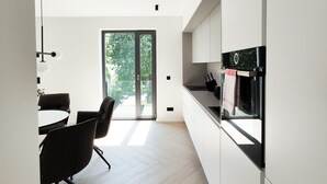 Een moderne keuken met een groot raam, een eethoek met stoelen en een vloer in een lichte kleur.