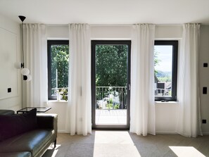 Un salon moderne avec un canapé en cuir noir, une petite table et une grande fenêtre ornée de rideaux blancs.