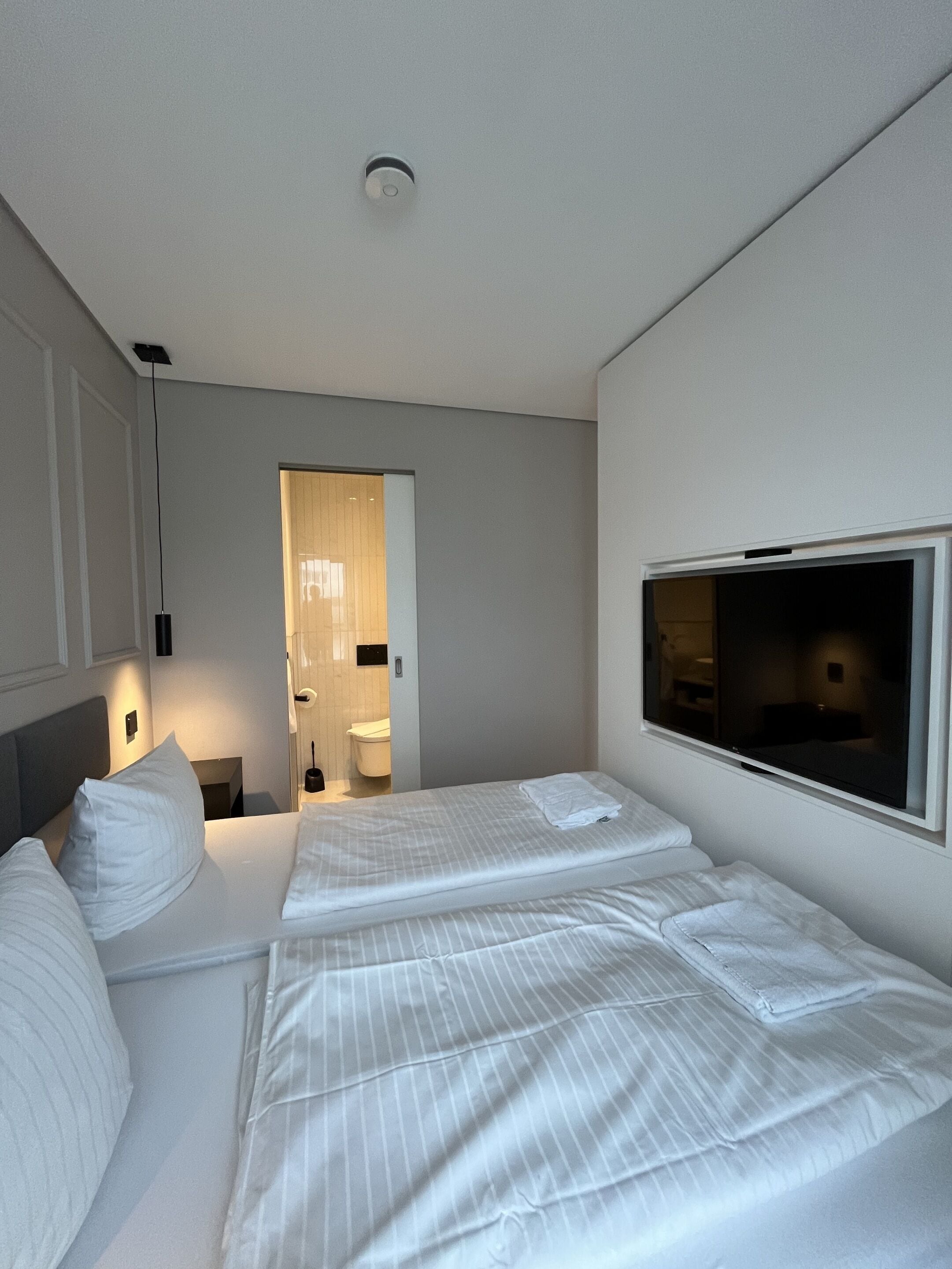 Habitación de hotel con una cama, un televisor y un baño visible a través de una puerta abierta.