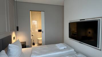 Habitación de hotel con una cama, un televisor y un baño visible a través de una puerta abierta.