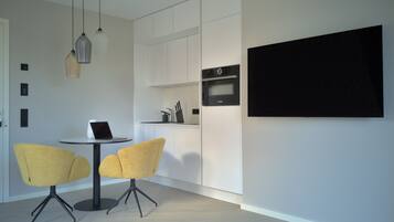 A modern kitchen with white cabinets, a Bosch oven, and a dining area with two yellow chairs and a laptop on a small table.