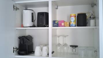 A kitchen with a coffee maker, a kettle, a box of coffee pods, a container of coffee creamer, and a set of wine glasses.