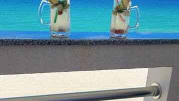 Deux boissons sur un balcon avec vue sur l’océan et une table avec des raisins.