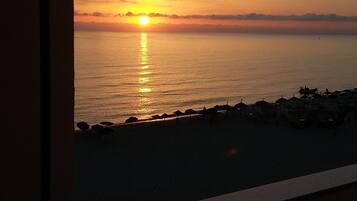 Un coucher de soleil sur une plage, avec vue sur la mer et une rangée de parasols de plage.