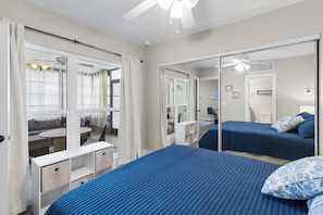 A hotel room with a large bed, a desk, a chair, a mirror, and a ceiling fan. - Pickleball, Pools & Docks - Yacht Club #165A (Madeira Beach)