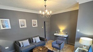 En moderne stue med en grå sofa, et sofabord og en grå lænestol. Der er en dør i baggrunden og en lampe på et sofabord.