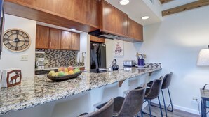 A kitchen with wooden cabinets, a granite countertop, and a fruit bowl. - NEW! Mountain Condo, Outdoor Hot Tubs, Stunning Summer Views - 201C (Frisco)