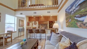 A spacious living area with a high ceiling, a dining table, a sofa, and a kitchen in the background. - NEW! Mountain Condo, Outdoor Hot Tubs, Stunning Summer Views - 201C (Frisco)