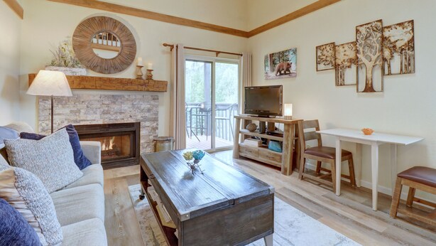 A living room with a fireplace, a TV, and a dining area with a table and chairs. - NEW! Mountain Condo, Outdoor Hot Tubs, Stunning Summer Views - 201C (Frisco)