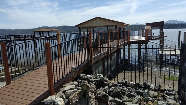 A wooden deck with a metal railing overlooking a body of water, a stone sculpture, and a small pavilion. - STUNNING  Lakefront,  Huge DOCK,2 Kayaks, Sleep 8, Prime fishing spot (Clearlake Oaks)