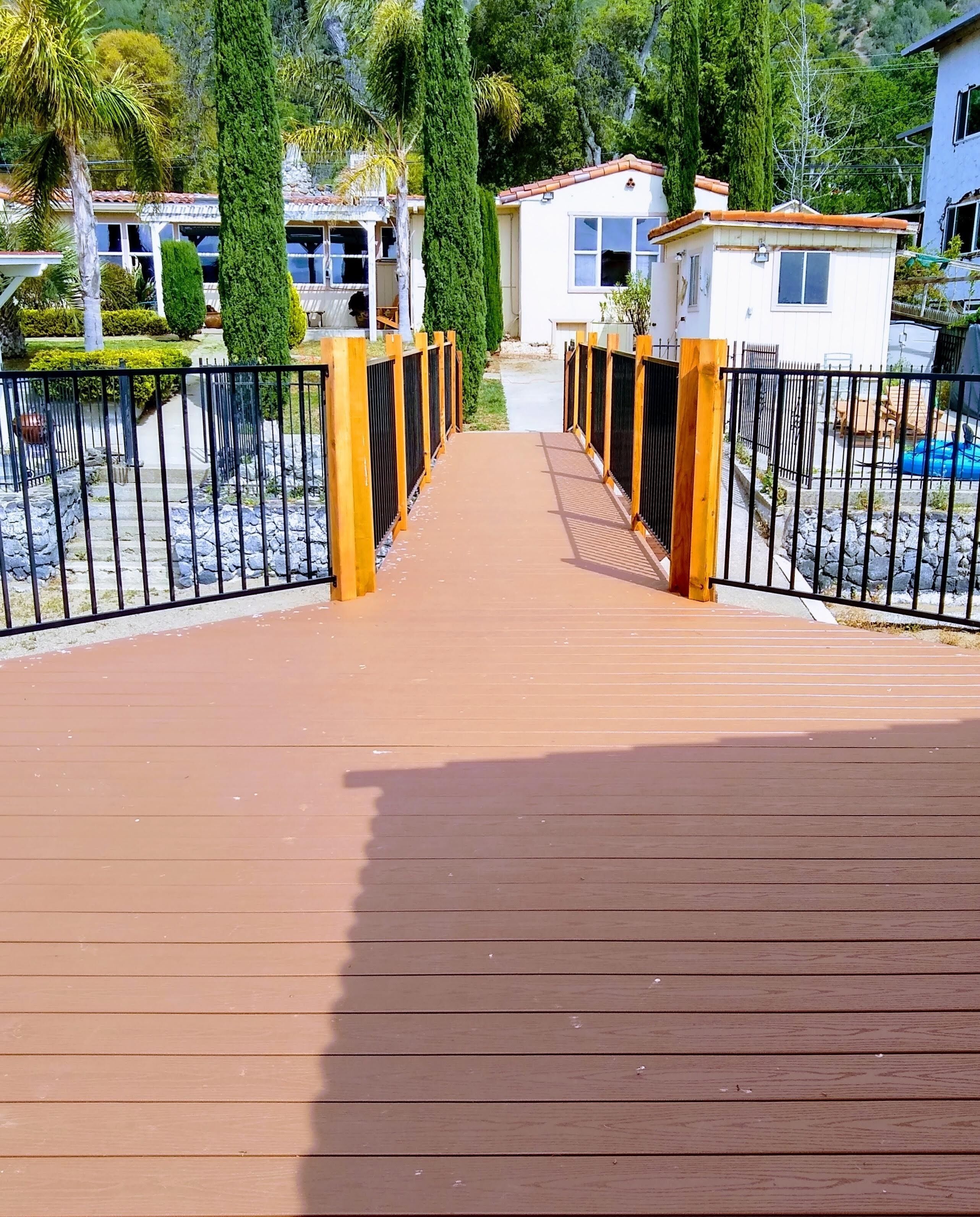 Une terrasse en bois mène à une entrée fermée par un portail, et un chemin en pierre y donne accès.