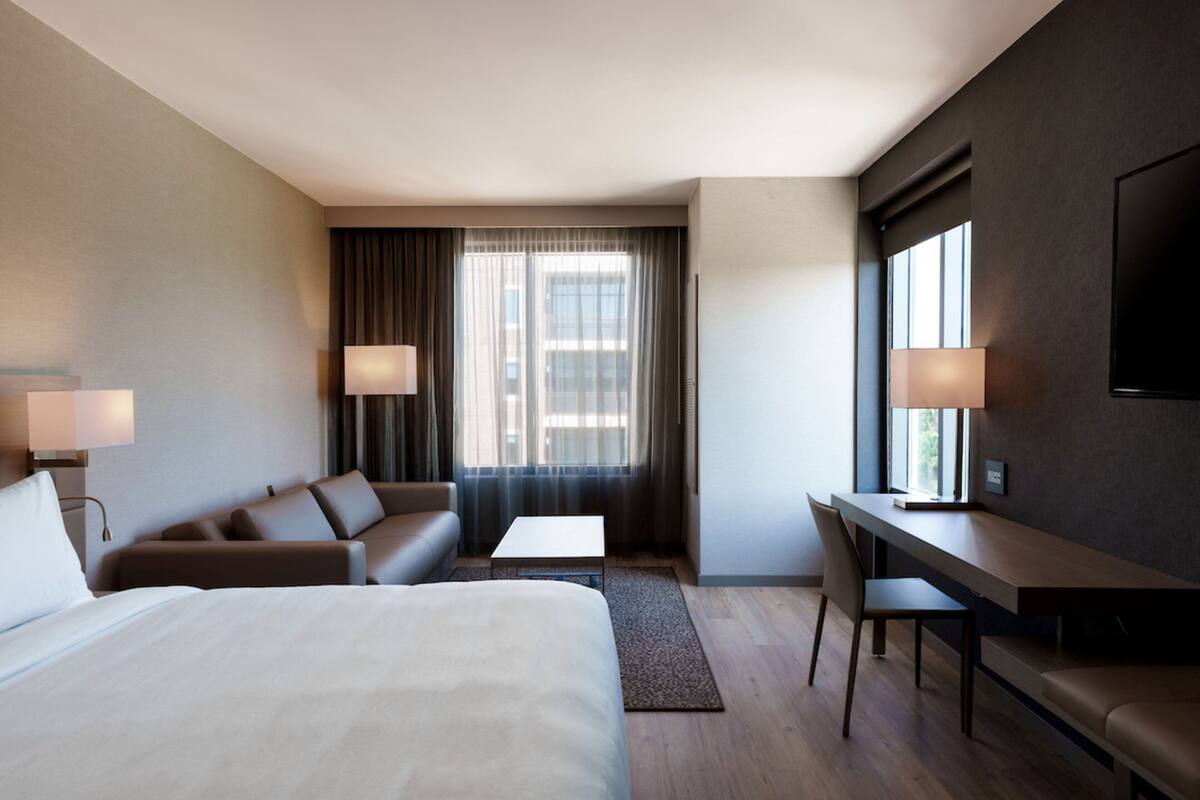 A modern hotel room with a large bed, a sofa, a desk, and a TV.