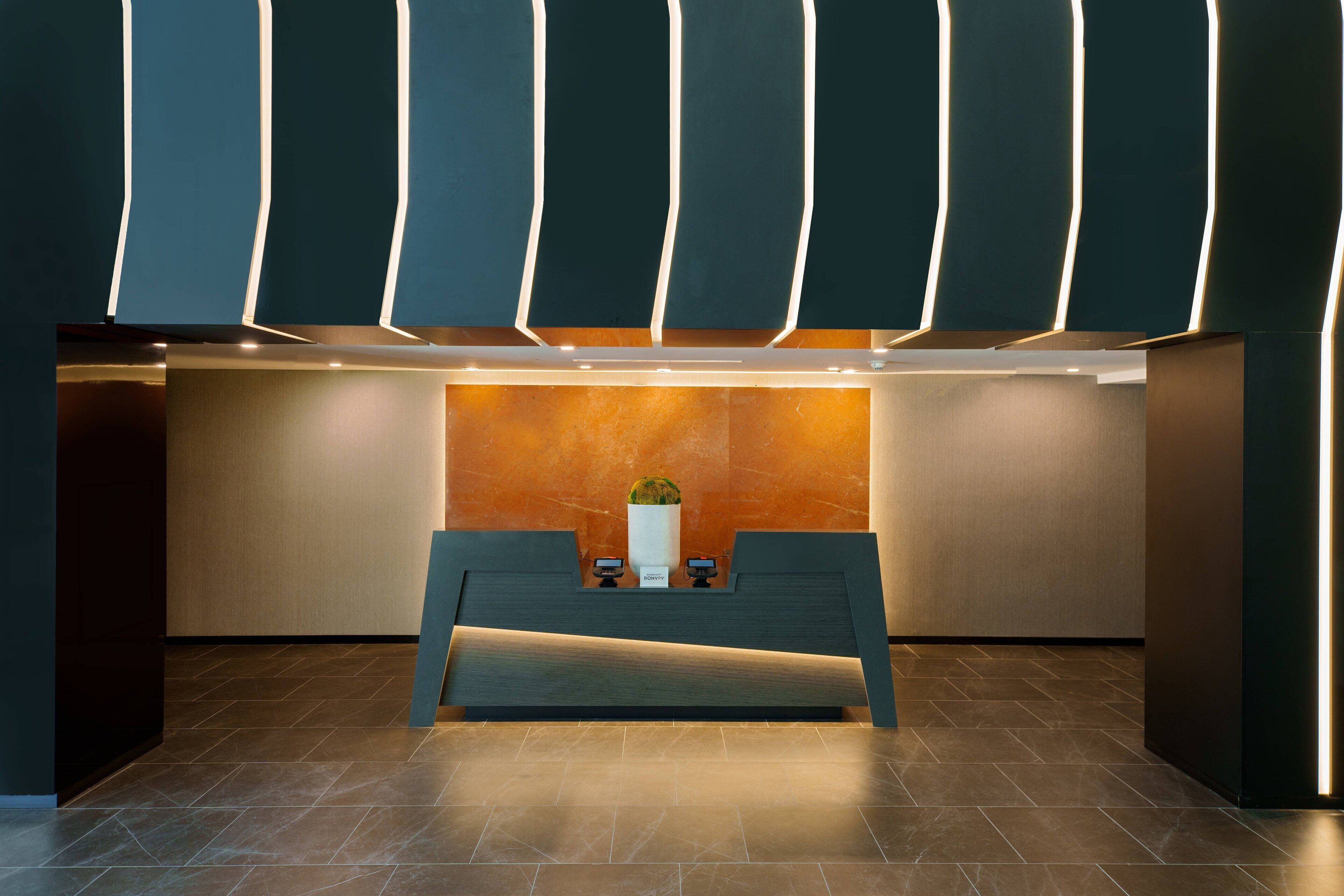 A reception desk with a modern design, a vase with a plant, and a wall with vertical light strips.