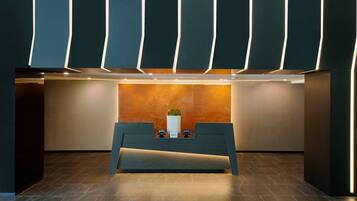 A reception desk with a modern design, a vase with a plant, and a wall with vertical light strips.