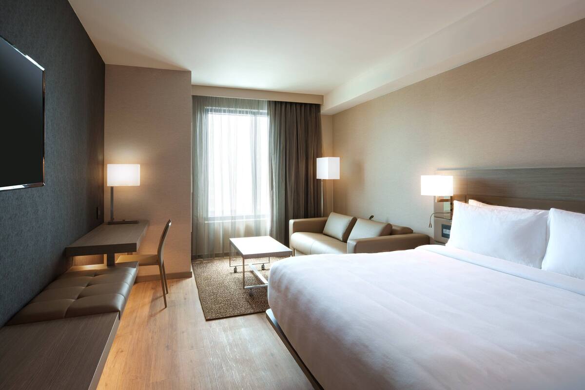 A hotel room with a large bed, a sofa, a desk, and a TV.