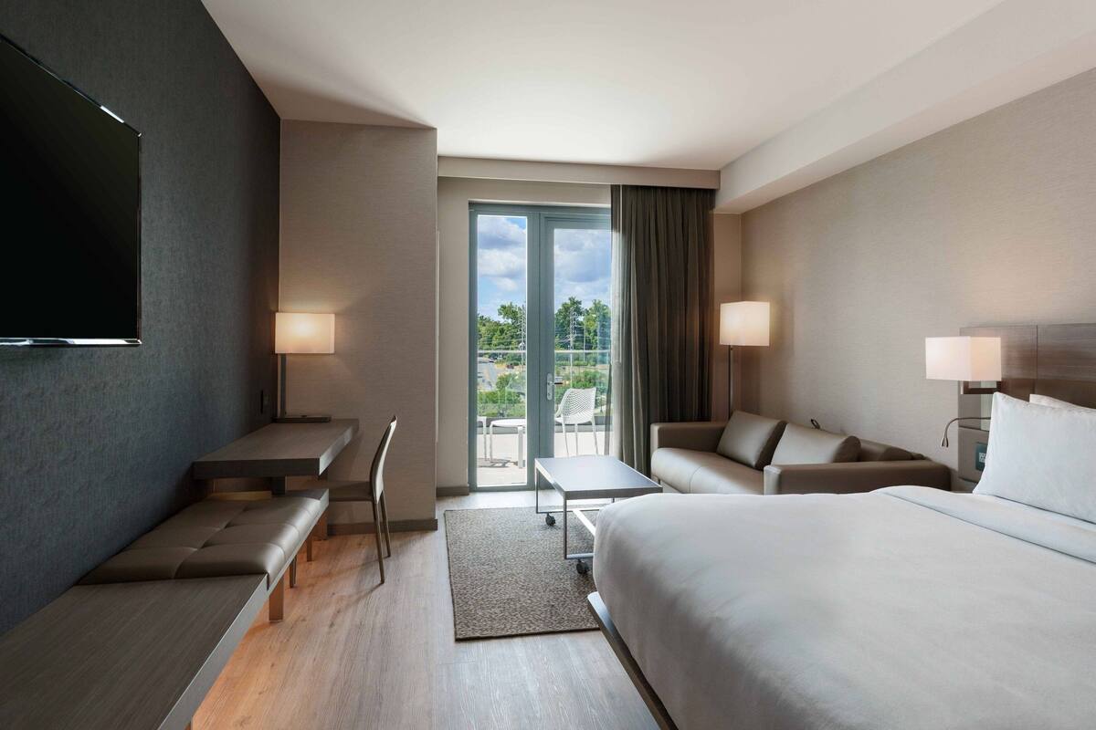 A modern hotel room with a large bed, a sofa, a desk, and a TV.