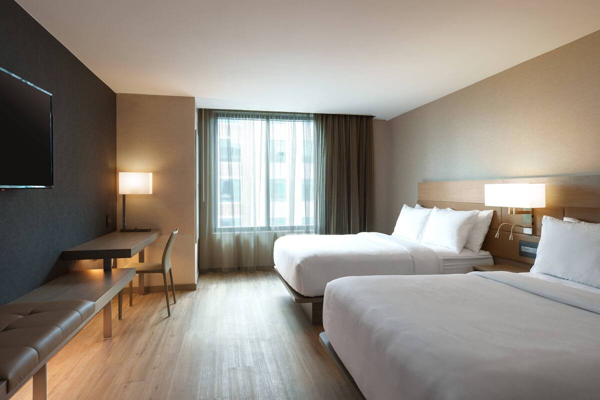A hotel room with two beds, a desk, a chair, a TV, and a window with curtains.