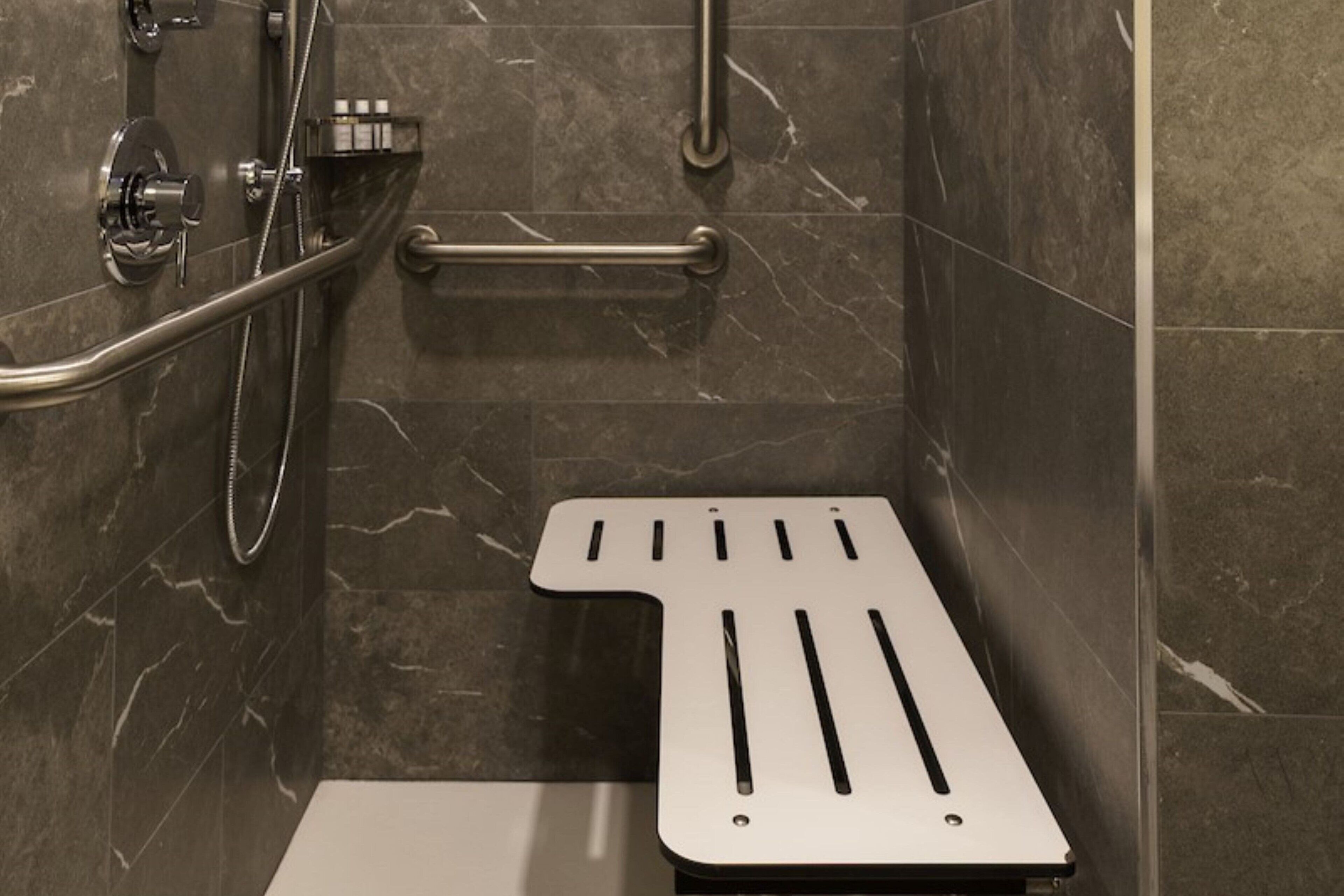 A shower area with a handheld showerhead, a handheld shower hose, and a grab bar.