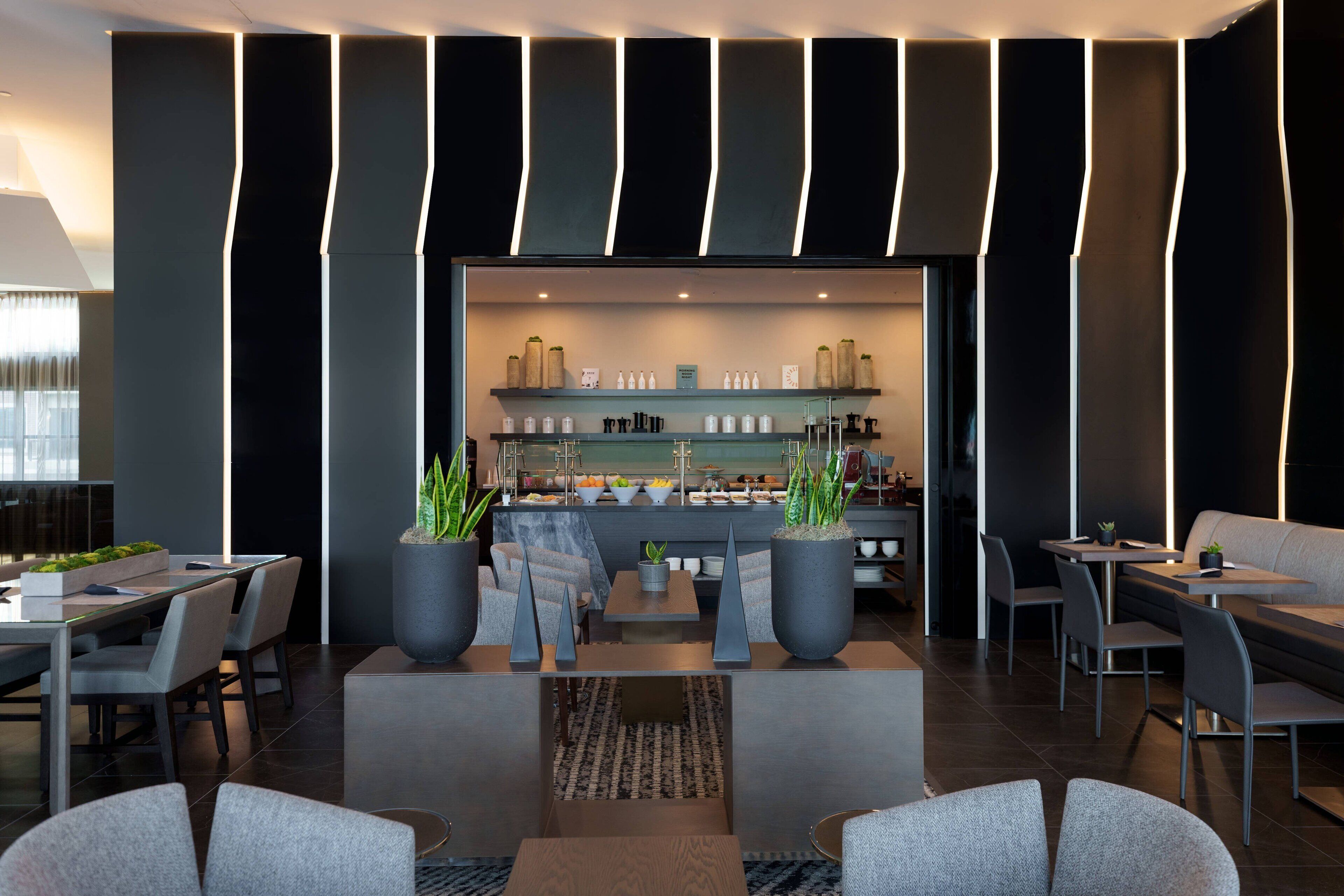 A modern hotel lobby with a bar area, seating arrangements, and potted plants.