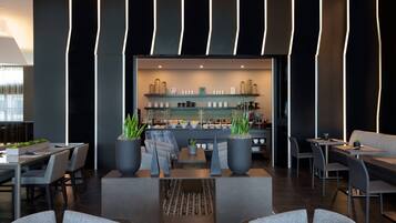 A modern hotel lobby with a bar area, seating arrangements, and potted plants.