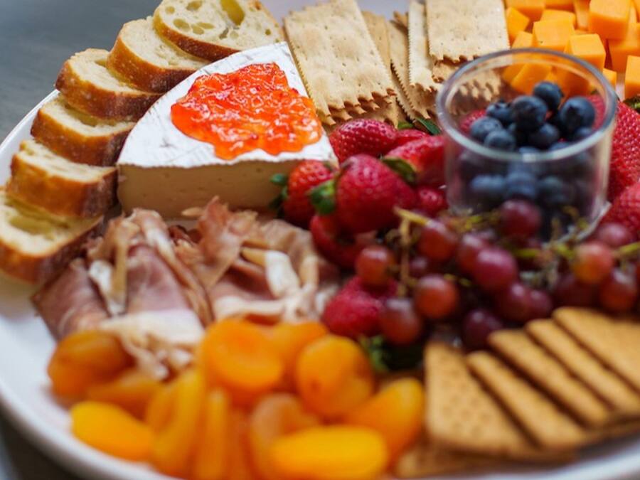A plate with various cheeses, fruits, and crackers.