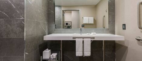 Une salle de bain moderne avec un grand miroir, un lavabo blanc et des carreaux de marbre foncé.