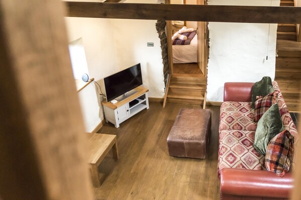 Ein gemütliches Zimmer mit Holzboden, einem Fernsehgerät auf einem weißen Schrank, einem roten Sofa mit gemusterten Kissen und einer kleinen Holzbank.