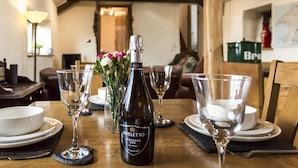 A dining table set with wine glasses, a bottle of Adèletto Prosecco, and a vase of flowers. - Foxglove - Barn Conversion - Blossom  Farm (Haverfordwest)