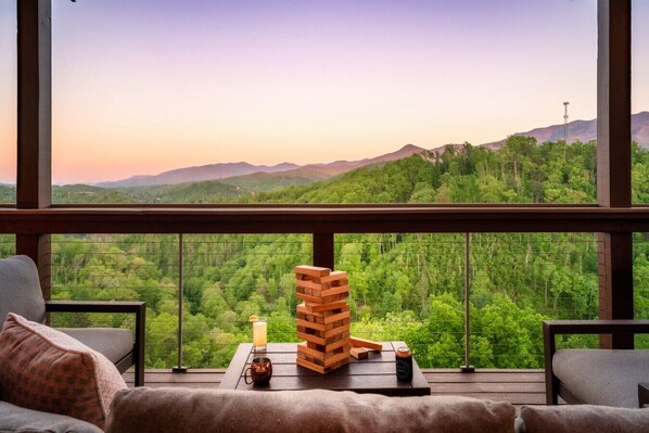 A room with a view of a forested mountain range, a stack of wooden blocks, a glass of orange juice, and a mug on a table.