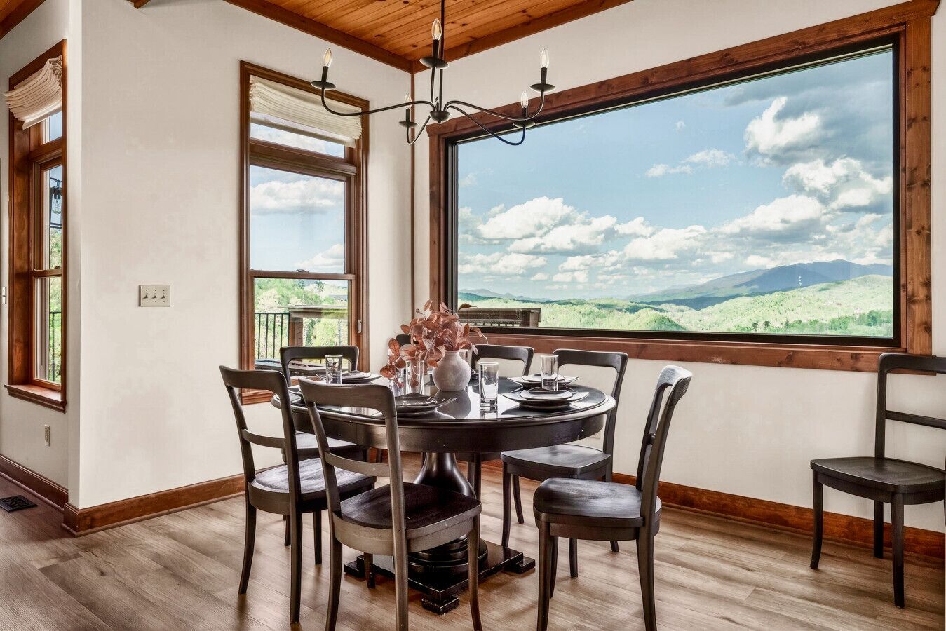 Comedor con mesa para cuatro, ventanas amplias con vista a la montaña y una araña.