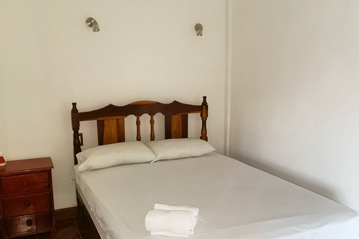 A single bed with a wooden headboard, a nightstand with drawers, and a white bedspread.