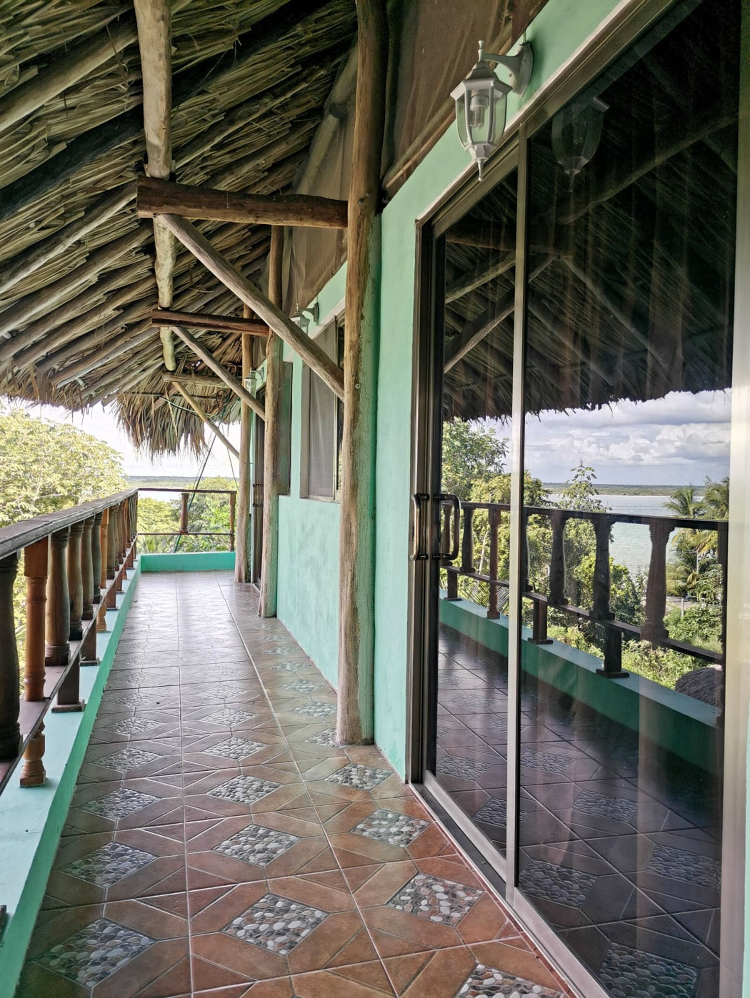 A covered balcony with a tiled floor and a railing, overlooking a scenic landscape.