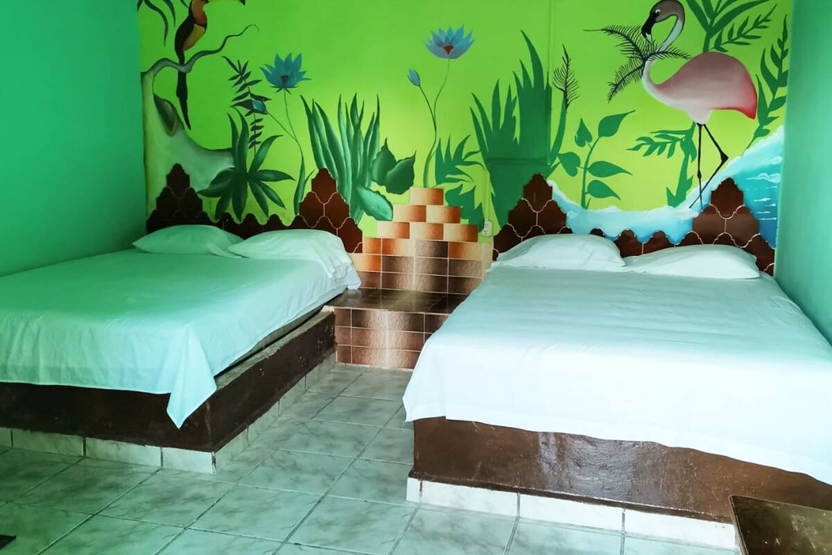 A room with two beds, green walls, and a mural of a tropical scene.
