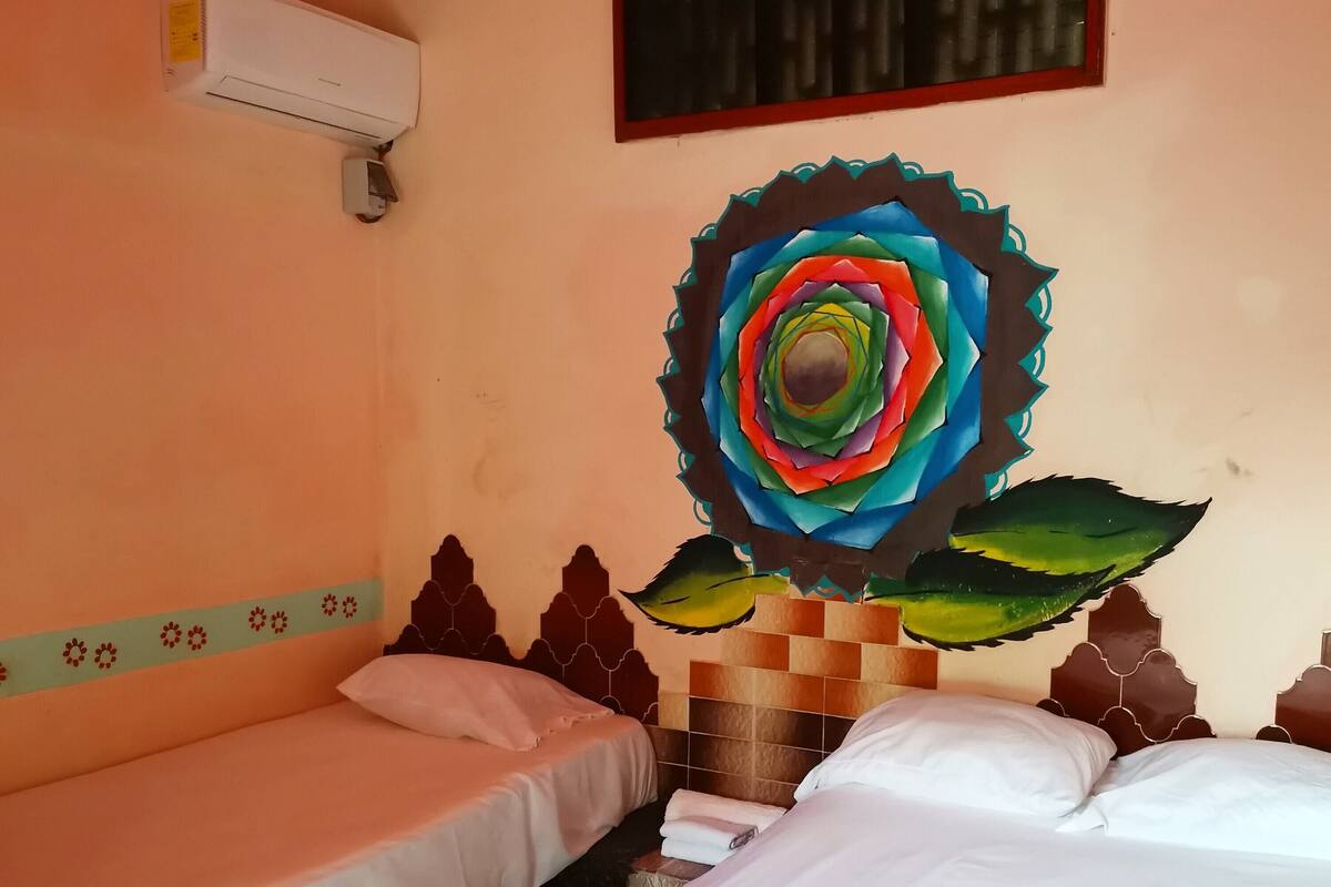 A room with two beds, a wall-mounted air conditioner, and a colorful floral artwork.