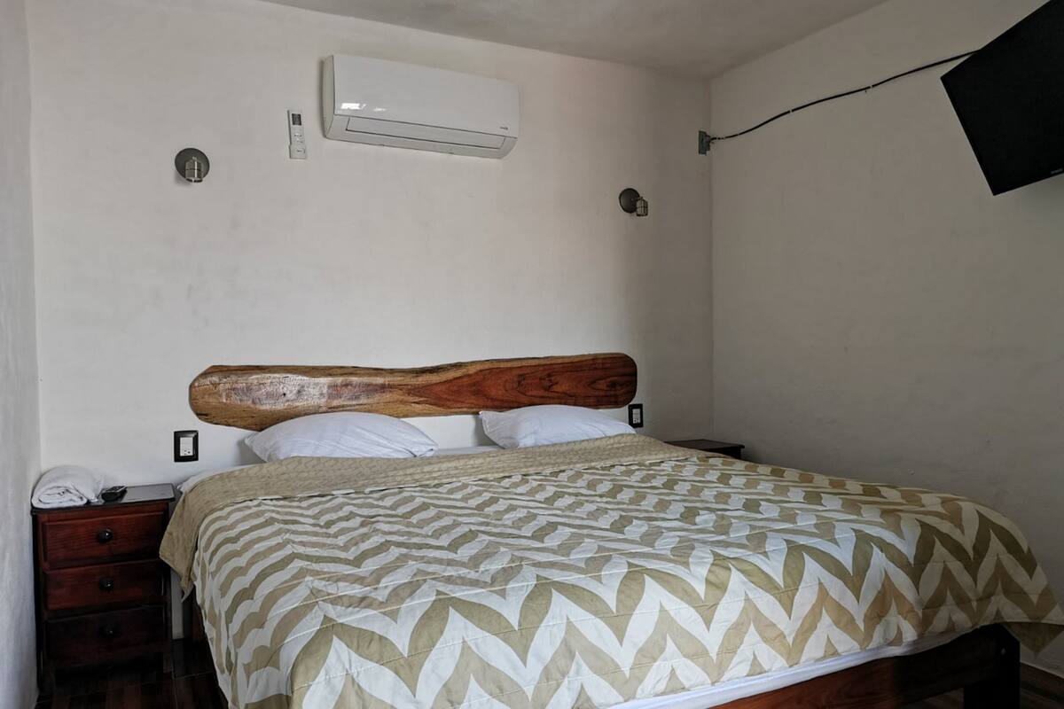 A bedroom with a wooden headboard, a bed with a patterned bedspread, a nightstand with a phone, and a wall-mounted air conditioner.