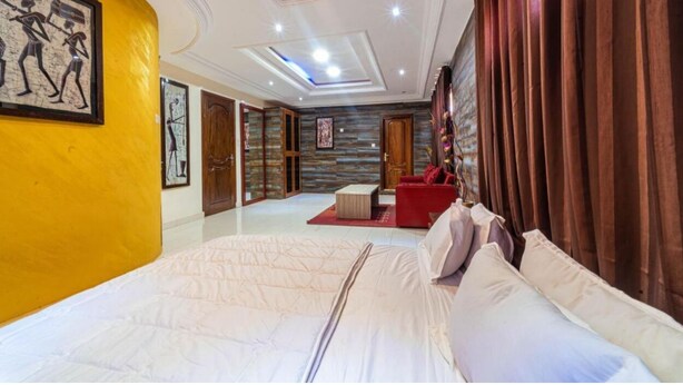 Une chambre d’hôtel avec un grand lit, un canapé rouge, une armoire en bois et un tableau au mur.