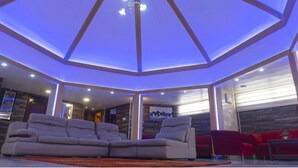 Un salon moderne doté d’un plafond au design original, d’un canapé d’angle et de fauteuils rouges.