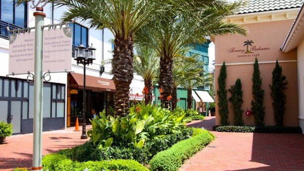 A well-maintained outdoor area with palm trees, a brick pathway, and a building labeled "Tommy Bahama Tropical Café." - Calabay Parc by PRP (Davenport)