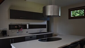 A modern kitchen with a central island, black cabinets, a stainless steel range hood, and a window with a view of trees.