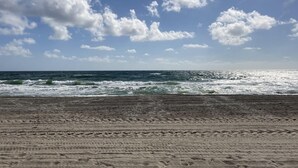 A beach with visible footprints in the sand, a clear sky, and waves approaching the shore. - 1 BR - Guesthouse - A beachside gem! Walk 1 min to Beach! (Boca Raton)